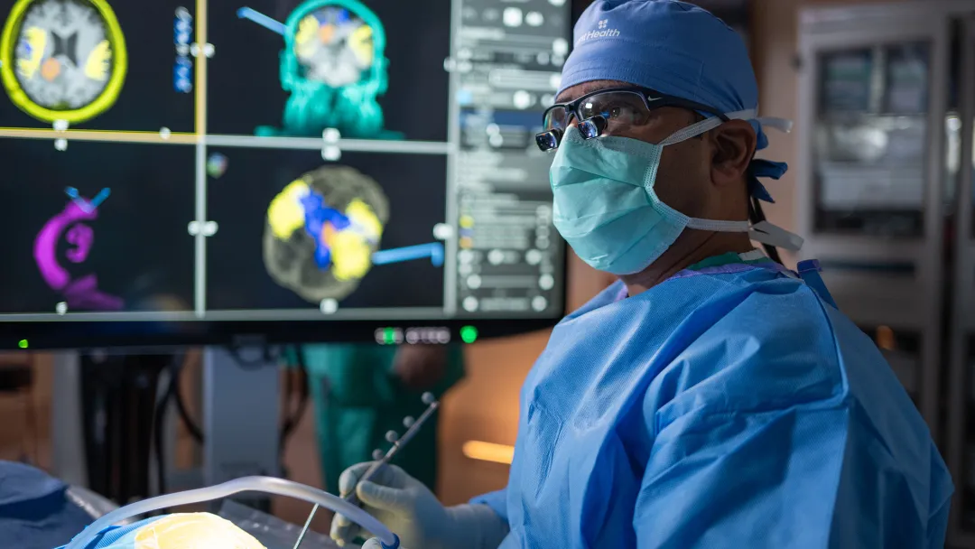 Surgeon at AdventHealth operating on a patients brain. A series of brain scans are located on the monitor behind him.