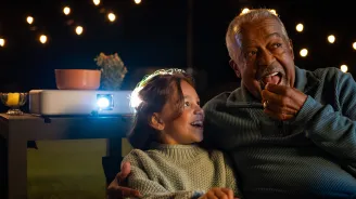 Grandfather watching a movie outdoors with his granddaughter.