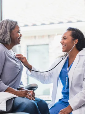 Doctor listening to an older woman patient's heart.