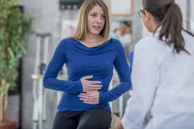 Woman with a stomach ache describes her symptoms to her doctor. 