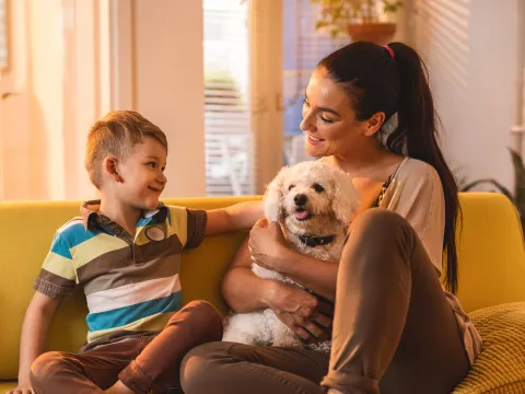 A Mother Sits on a Couch with Her Son and a Dog in Her Lap