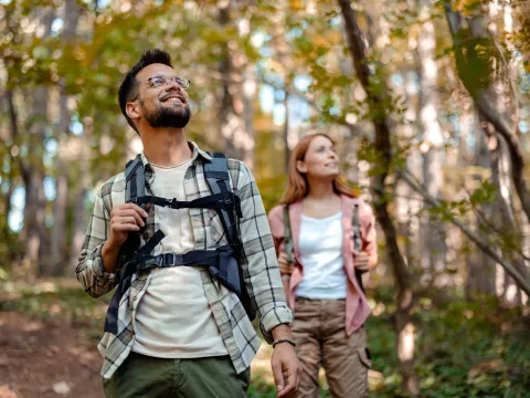 A man and woman with backpacks walking in the woods.