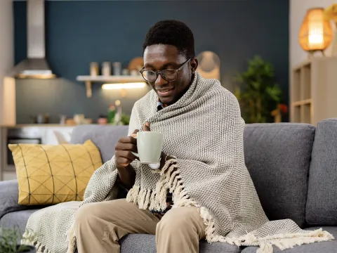 Man wrapped in blanket with cup of coffee while sitting on sofa
