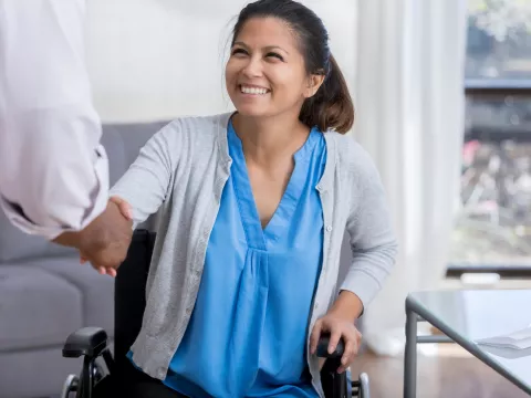 A woman in a wheelchair is shaking hands with a doctor.
