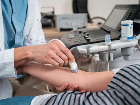 At the medical clinic, unrecognizable Caucasian male doctor doing the doppler ultrasound test evaluation of arteries and veins on a senior female patient