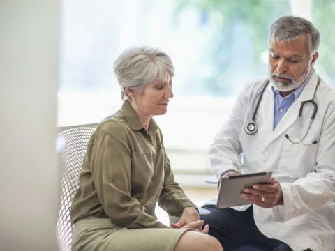 senior man doctor medical professional talks using digital tablet to senior woman in health clinic - stock photo
