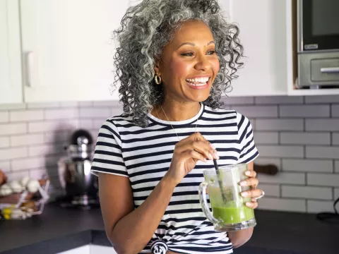 A woman drinking a healthy green smoothie in her kitchen.