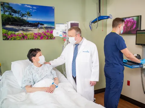 Patient in hospital bed talking with doctor and nurse charting.