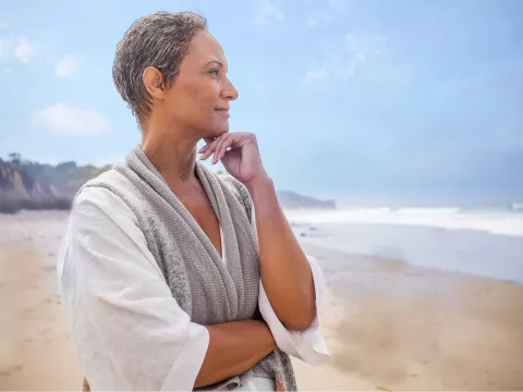 An adult woman stands on the beach and looks out at the ocean