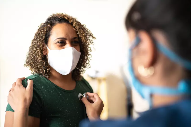 A Woman Wearing a Face Mask has her Vitals Taken by a Care Provider