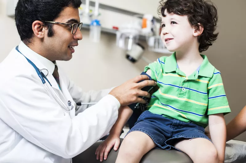 A child, sitting on an exam table, as a doctor takes his blood pressure.