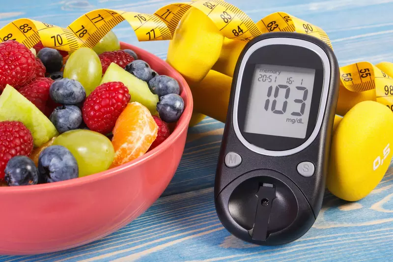 A bowl of fresh fruit next to a blood sugar monitor