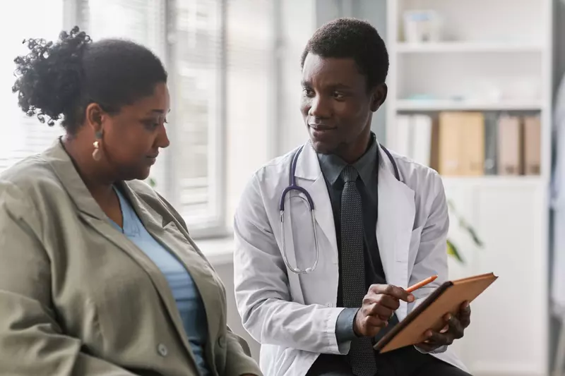 A black woman patient talks with a black male doctor.