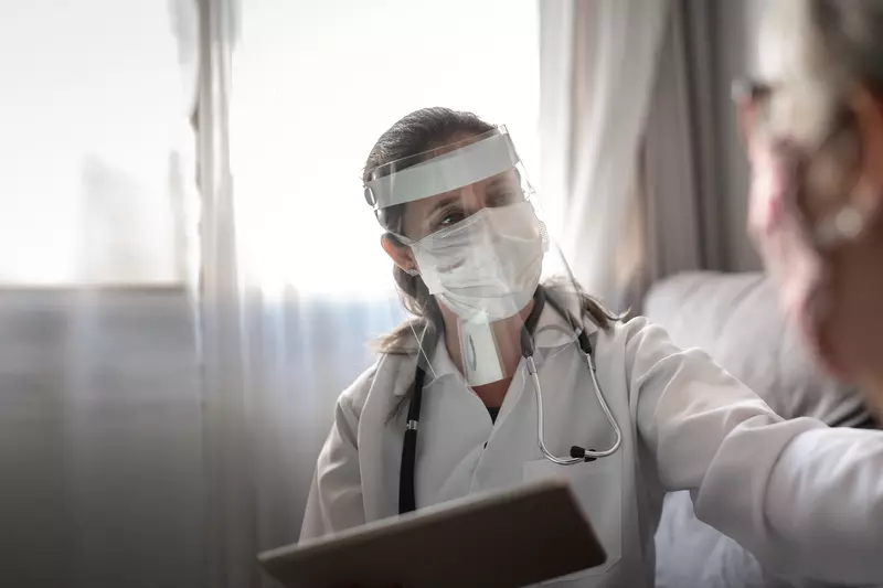 Doctor wearing PPE and talking with a patient that's wearing a mask.