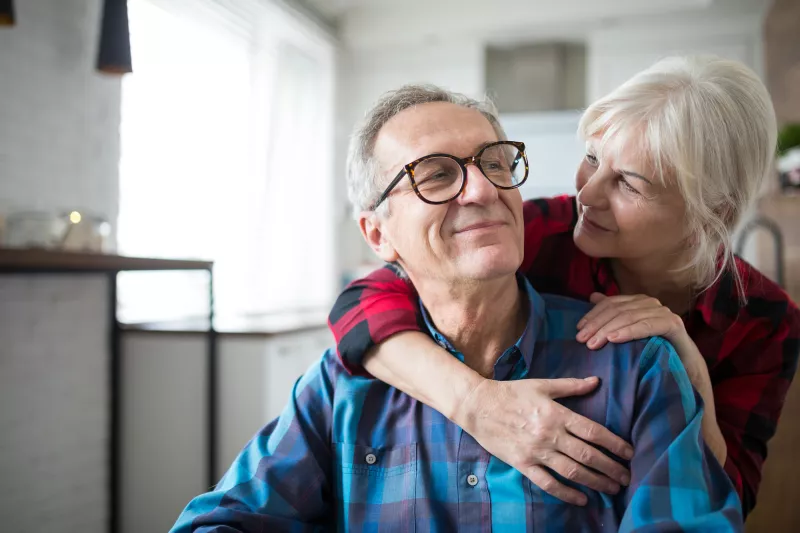 A senior man smiles at his wife as they embrace