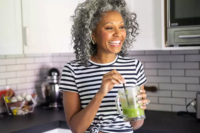 A woman drinking a healthy green smoothie in her kitchen.