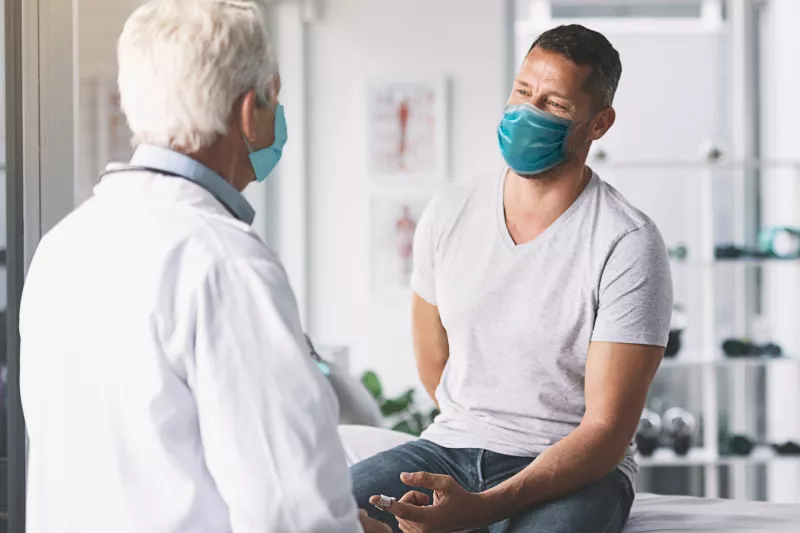 Man talking with talking while both are wearing masks.