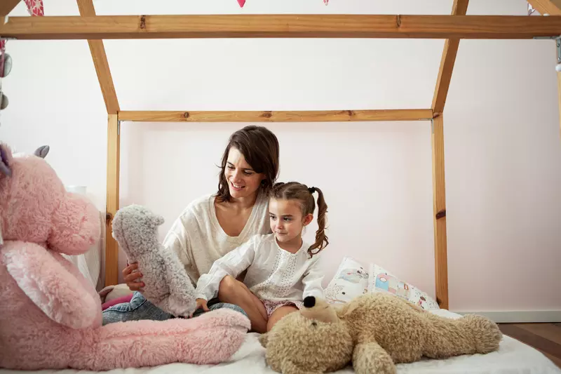 Mother and daughter on a bed with stuffed animals.