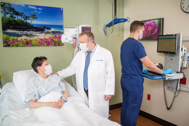 Patient in hospital bed talking with doctor and nurse charting.
