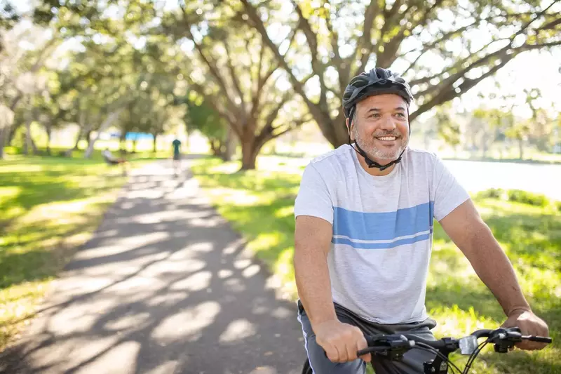 Smiling man riding his bike through the park.
