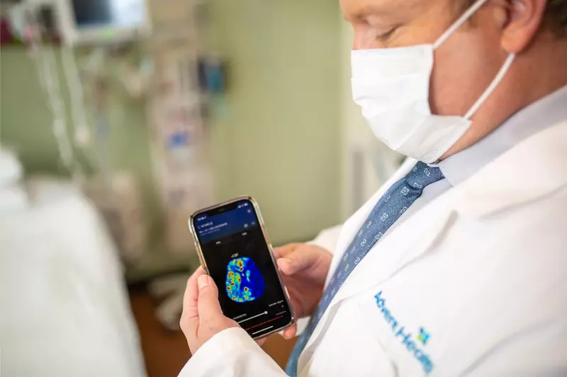 Physician holding a smartphone with a brain scan on screen.