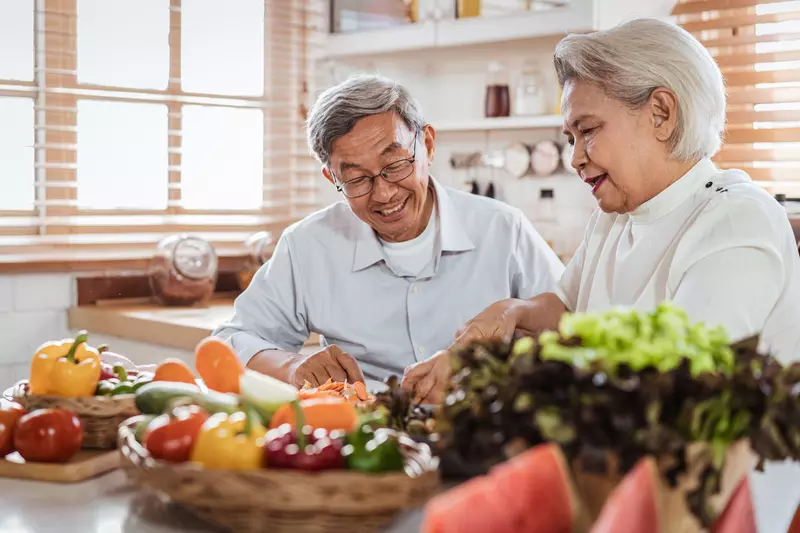 Senior couple sitting at the kitchen counter with produce on the kitchen table.