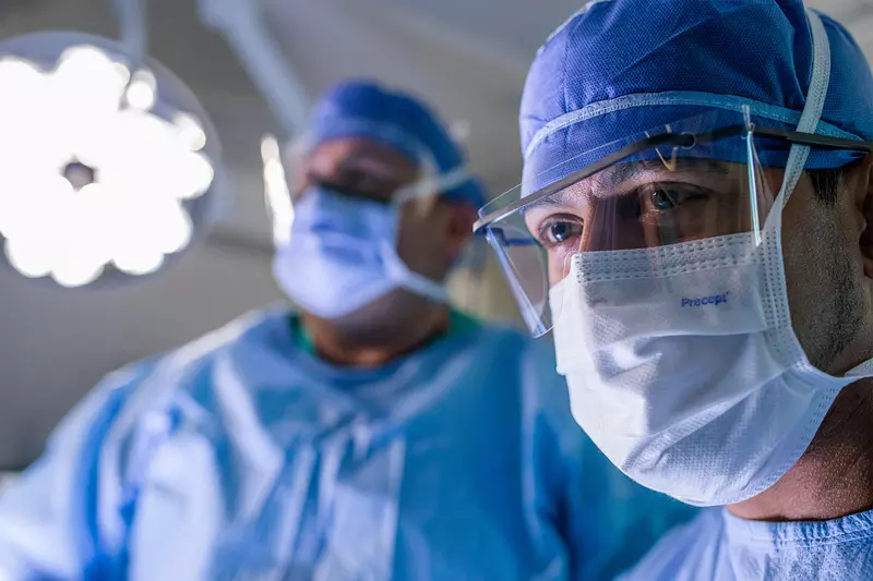 Close up of a surgeon in the foreground with another surgeon in the background in the operating room during a surgery.
