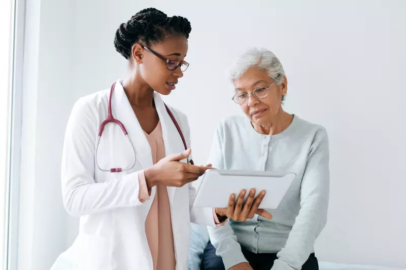 An older female patient and her physician look at a chart.