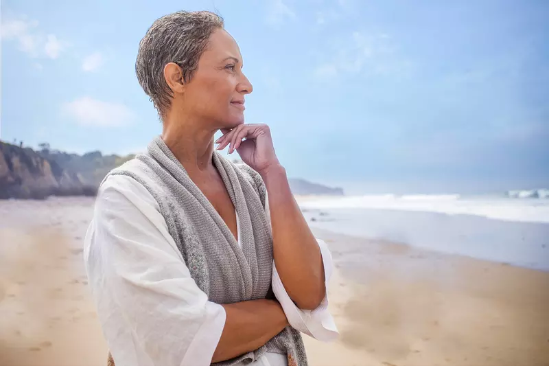 An adult woman stands on the beach and looks out at the ocean