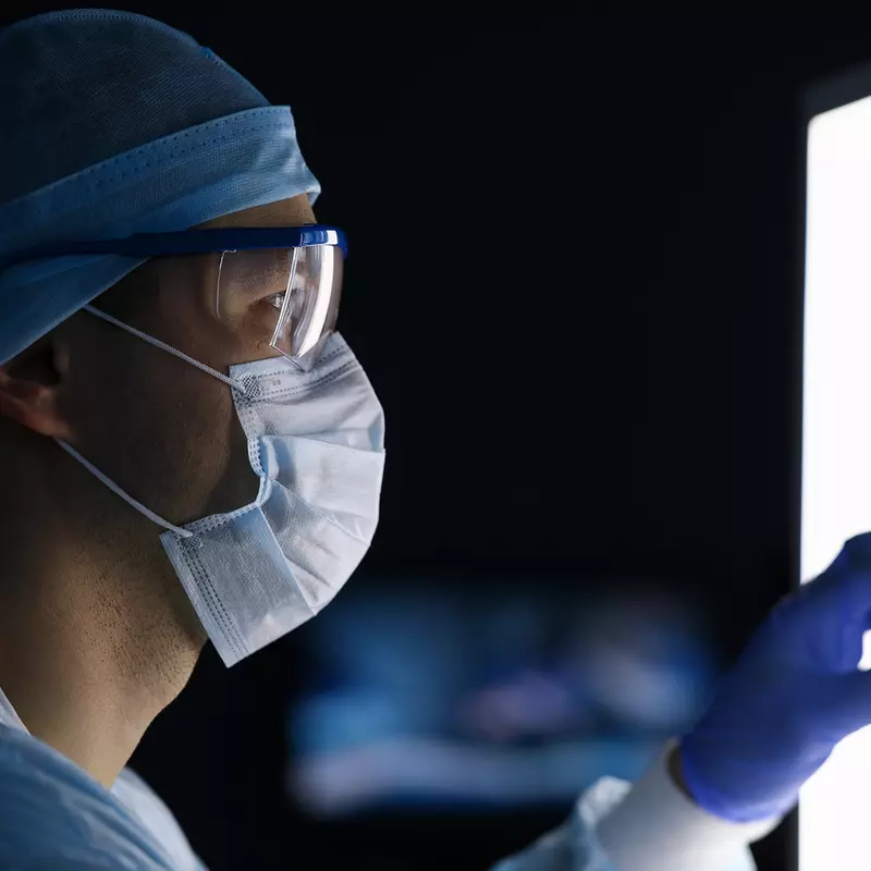 A Doctor, in Full Scrubs and Face Mask, Looks Over His Patient's Scans