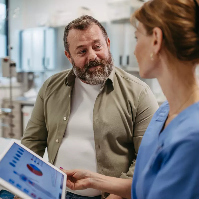 A Patient Speaks to a Provider in an Exam Room as She Goes Over His Vitals on a Tablet