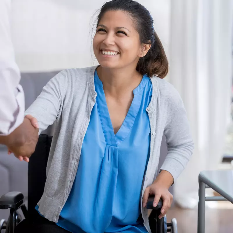 A woman in a wheelchair is shaking hands with a doctor.