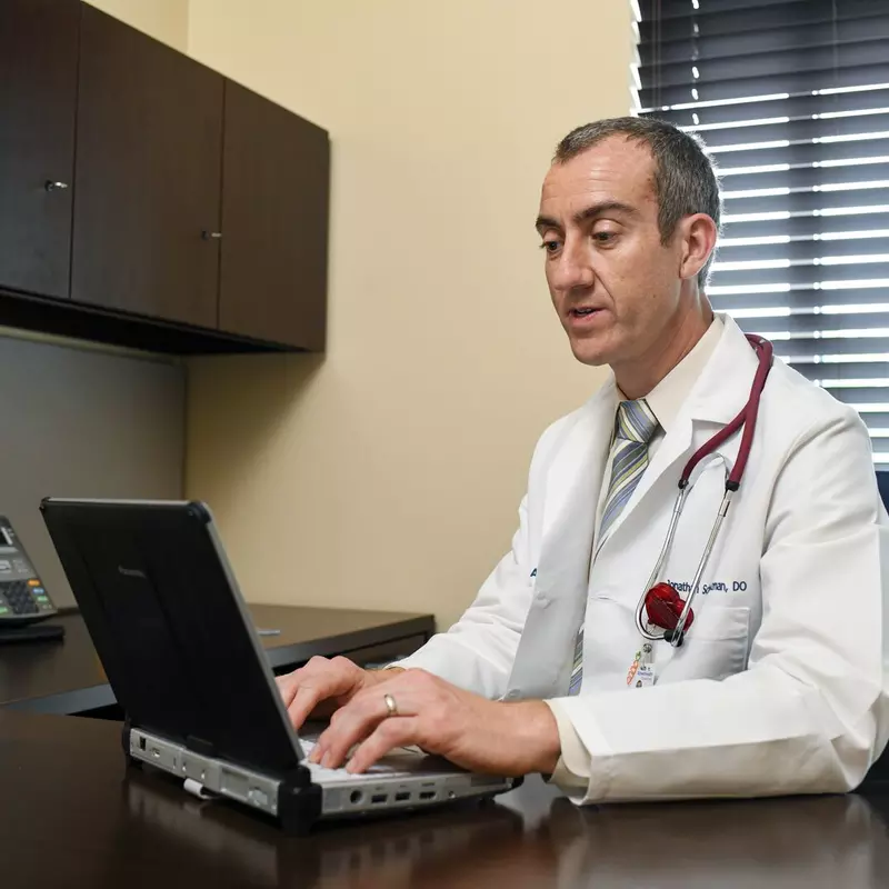 Physician at desk in white coat typing on laptop
