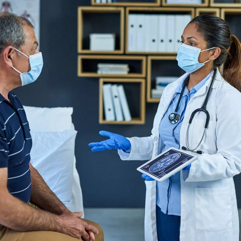 A masked doctor talking to her masked patient with a tablet on her hand