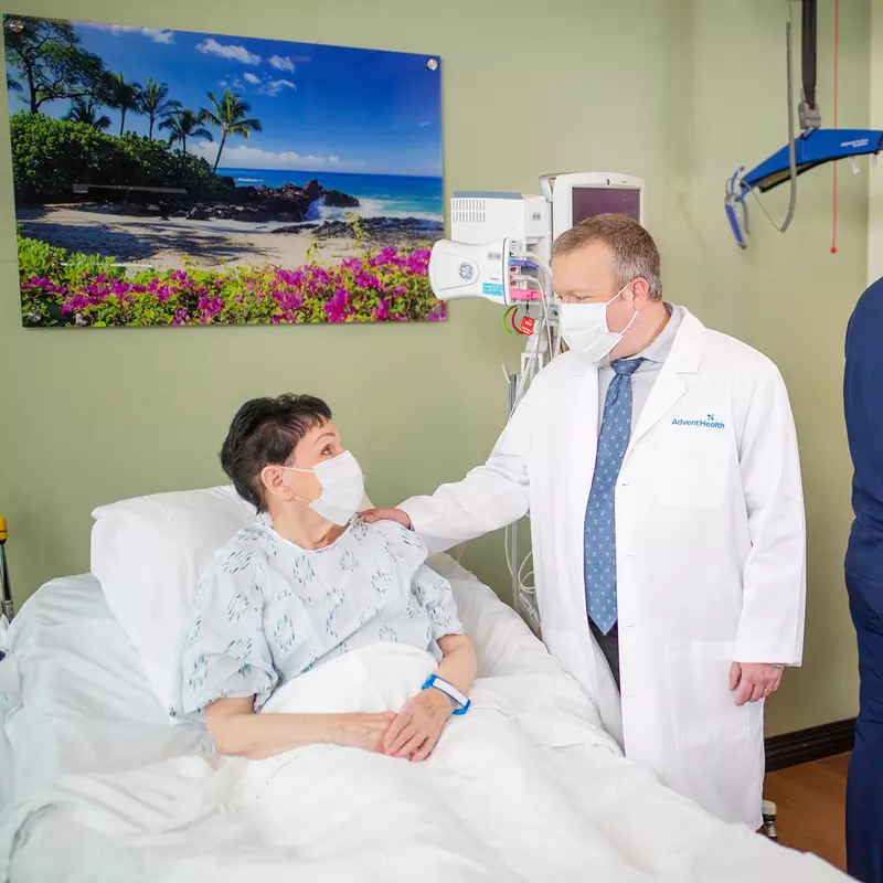 Patient in hospital bed talking with doctor and nurse charting.