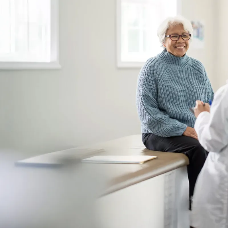 An older female patient talking to a female physician in an exam room.