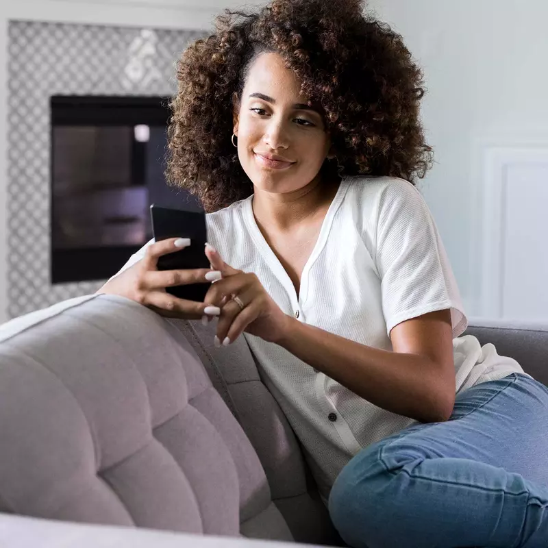 A woman on her cell phone at home on her couch. 