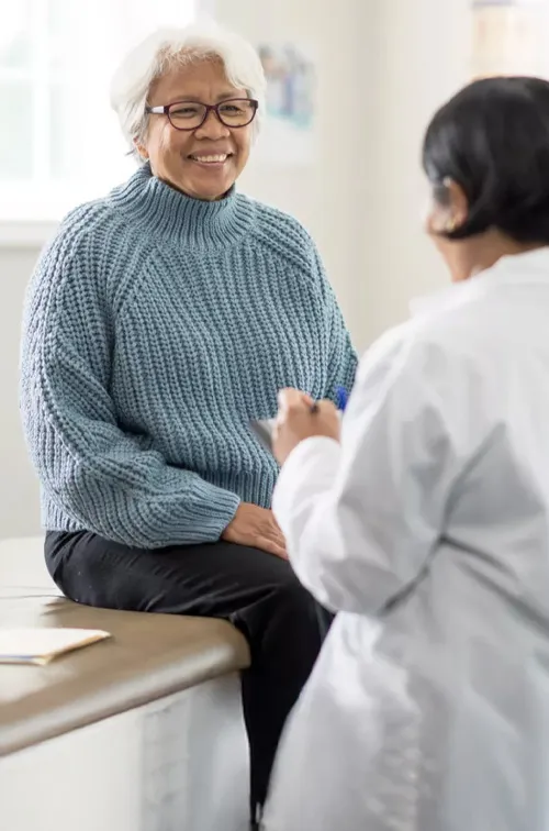 An older female patient talking to a female physician in an exam room.